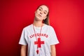 Beautiful lifeguard woman wearing t-shirt with red cross using whistle over isolated background looking sleepy and tired,