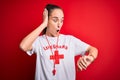 Beautiful lifeguard woman wearing t-shirt with red cross using whistle over isolated background Looking at the watch time worried,
