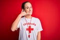 Beautiful lifeguard woman wearing t-shirt with red cross using whistle over isolated background smiling doing phone gesture with