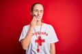 Beautiful lifeguard woman wearing t-shirt with red cross using whistle over isolated background touching mouth with hand with