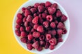 a beautiful light blue bowl of fruit with raspberries, blueberries and blackberries on yellow background, top view, studio shot Royalty Free Stock Photo