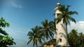 Beautiful lighthouse with palm trees on shore of tropical bay. Action. Beautiful bay shore with lighthouse and palm