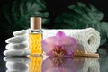 Lilac orchid flower, clear bottle of yellow oil, wooden sticks and towel with white stones and monstera on black surface Royalty Free Stock Photo