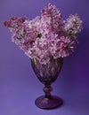 Beautiful lilac vintage faceted glass on a table with lilac flowers on a purple background