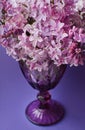 Beautiful lilac vintage faceted glass on a table with lilac flowers on a purple background