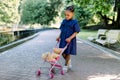 Beautiful little African girl in blue dress is playing with teddy bear toy, sitting in small kid stroller, walking in Royalty Free Stock Photo