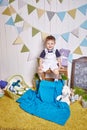 Beautiful little baby boy sitting on a chair with a knitted blanket Easter basket with colored eggs hay, Easter Bunny, a holy Royalty Free Stock Photo