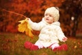Beautiful little baby girl sitting with a big leaf at autumn park