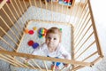 Beautiful little baby girl standing inside playpen. Cute adorable child playing with colorful toy Royalty Free Stock Photo