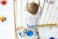 Beautiful little baby girl standing inside playpen. Cute adorable child playing with colorful toy Royalty Free Stock Photo