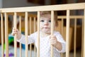 Beautiful little baby girl standing inside playpen. Cute adorable child playing with colorful toy Royalty Free Stock Photo