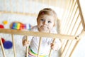 Beautiful little baby girl standing inside playpen. Cute adorable child playing with colorful toy Royalty Free Stock Photo