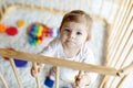 Beautiful little baby girl standing inside playpen. Cute adorable child playing with colorful toy Royalty Free Stock Photo