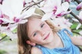 Beautiful little blond girl in blue dress holding flowers of magnolia under blossom magnolia tree. Royalty Free Stock Photo