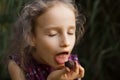 Beautiful little blond girl in violet dress with ponytail is eating a chocolate candy in the park durring a day, sugar Royalty Free Stock Photo