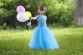 Beautiful little blond long-haired girl in nice long blue evening dress looking like princess looks in camera holding colorful ba Royalty Free Stock Photo