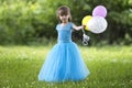 Beautiful little blond long-haired girl in nice long blue evening dress looking like princess looks in camera holding colorful bal Royalty Free Stock Photo