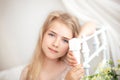 Beautiful little blonde girl with long hair sits on a bed with a bouquet of daisies in a bright white bedroom with a rustic interi