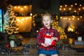 A beautiful little blonde girl received a sweet Christmas gift sitting on a wooden table in a decorated house Royalty Free Stock Photo