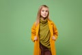 Beautiful little blonde kid girl 12-13 years old in yellow coat posing isolated on pastel green background children Royalty Free Stock Photo