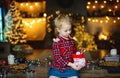 A beautiful little blonde received a sweet Christmas gift and laughs happily sitting on a wooden table in a decorated house Royalty Free Stock Photo