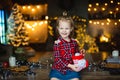 A beautiful little blonde received a sweet Christmas gift and laughs happily sitting on a wooden table in a decorated house Royalty Free Stock Photo