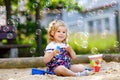 Beautiful little blonde toddler girl having fun with blowing soap bubble blower. Cute adorable baby child playing on Royalty Free Stock Photo