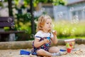 Beautiful little blonde toddler girl having fun with blowing soap bubble blower. Cute adorable baby child playing on Royalty Free Stock Photo