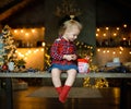 A beautiful little blonde in a traditional plaid shirt opens a chocolate bar from her sweet Christmas gift Royalty Free Stock Photo