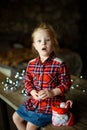 A beautiful little blonde girl received a sweet Christmas gift sitting on a wooden table in a decorated house Royalty Free Stock Photo