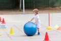 Beautiful little boy rolling the big blue ball on sports polygon