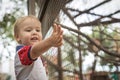 Beautiful little boy smiling standing at fence with animals in the zoo stretching forwards hand