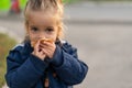 A beautiful little Caucasian girl with blond hair and eating bread eagerly with her hands looks at the camera with sad eyes