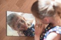 Beautiful little child girl with face painted with color tint in dress looking at her reflection in mirror on floor during self Royalty Free Stock Photo