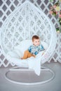 A beautiful little boy sits on a swing and poses for a photographer