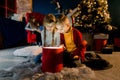 Beautiful little children look at a magical gift, their brothers and sisters read a book with Christmas stories and