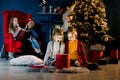 Beautiful little children look at a magical gift, their brothers and sisters read a book with Christmas stories and