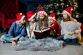 Beautiful little children read a book with Christmas stories on the background of a Christmas tree in red New Year hats