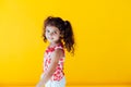 Beautiful little curly cheerful girl with pigtails on a yellow background