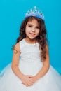 Beautiful little curly girl with crown tiara in white dress on a blue background background Royalty Free Stock Photo