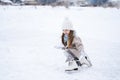 Beautiful little cute girl learn to skate on ice skating rink in park. Fall down and have fun. Stylish look, warm woolen coat, Royalty Free Stock Photo