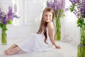 Beautiful little emotional girl siting among violet flowers. A flower decor in an interior