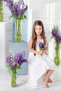 Beautiful little emotional girl sits among violet flowers. A flower decor in an interior