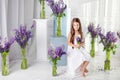 Beautiful little emotional girl sits among violet flowers. A flower decor in an interior