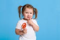 Beautiful little female child holding huge lollipop spiral candy smiling happy on blue background. Royalty Free Stock Photo