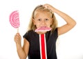 Beautiful little female child with sweet blue eyes and long blond hair eating huge lollipop spiral candy Royalty Free Stock Photo