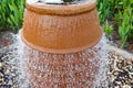 A beautiful little fountain in the form of a brown vase, a jug with falling drops of water on colored stones standing Royalty Free Stock Photo