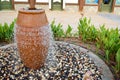 A beautiful little fountain in the form of a brown vase, a jug with falling drops of water on colored stones standing Royalty Free Stock Photo