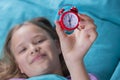 Beautiful little girl with alarm clock on bed in the bedroom.