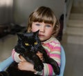 A beautiful little girl with blue eyes is holding a black cat. Friendship with pets. Royalty Free Stock Photo